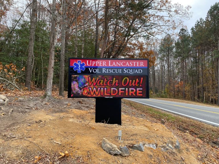 Outdoor LED sign from a volunteer rescue squad displaying wildfire warning message along a rural roadside with trees