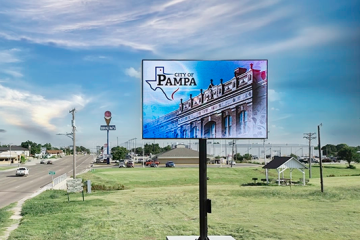Outdoor LED billboard displaying City of Pampa message beside a roadway with passing cars and open landscape