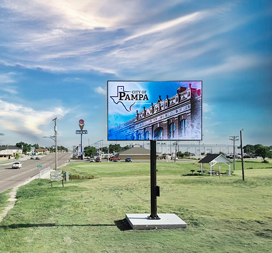 Outdoor LED billboard displaying City of Pampa message beside a roadway with passing cars and open landscape