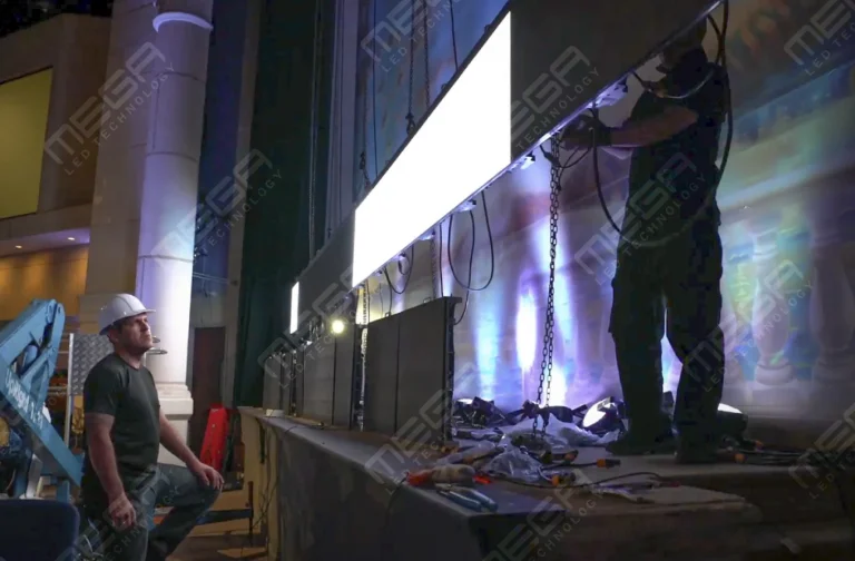 Technicians installing a large LED display panel on a stage inside an indoor theater