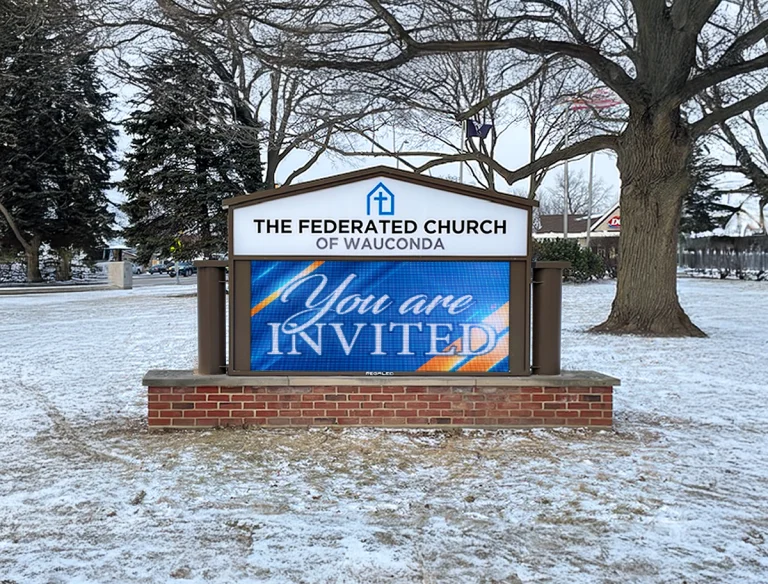 Outdoor LED sign at a church displaying welcome message in a snowy roadside setting with trees and open space in Washington