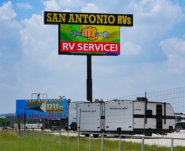 Outdoor LED sign displaying RV service advertisement at a roadside RV dealership location with trailers and open sky