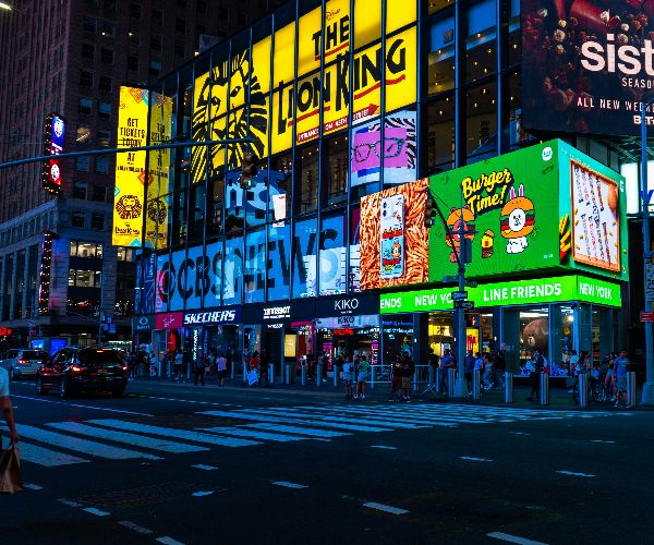 Multiple large digital LED billboards displaying advertisements on buildings in a busy urban Times Square street at night