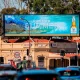 Outdoor LED billboard displaying beverage advertisement above a busy roadway with traffic and retail buildings in the background